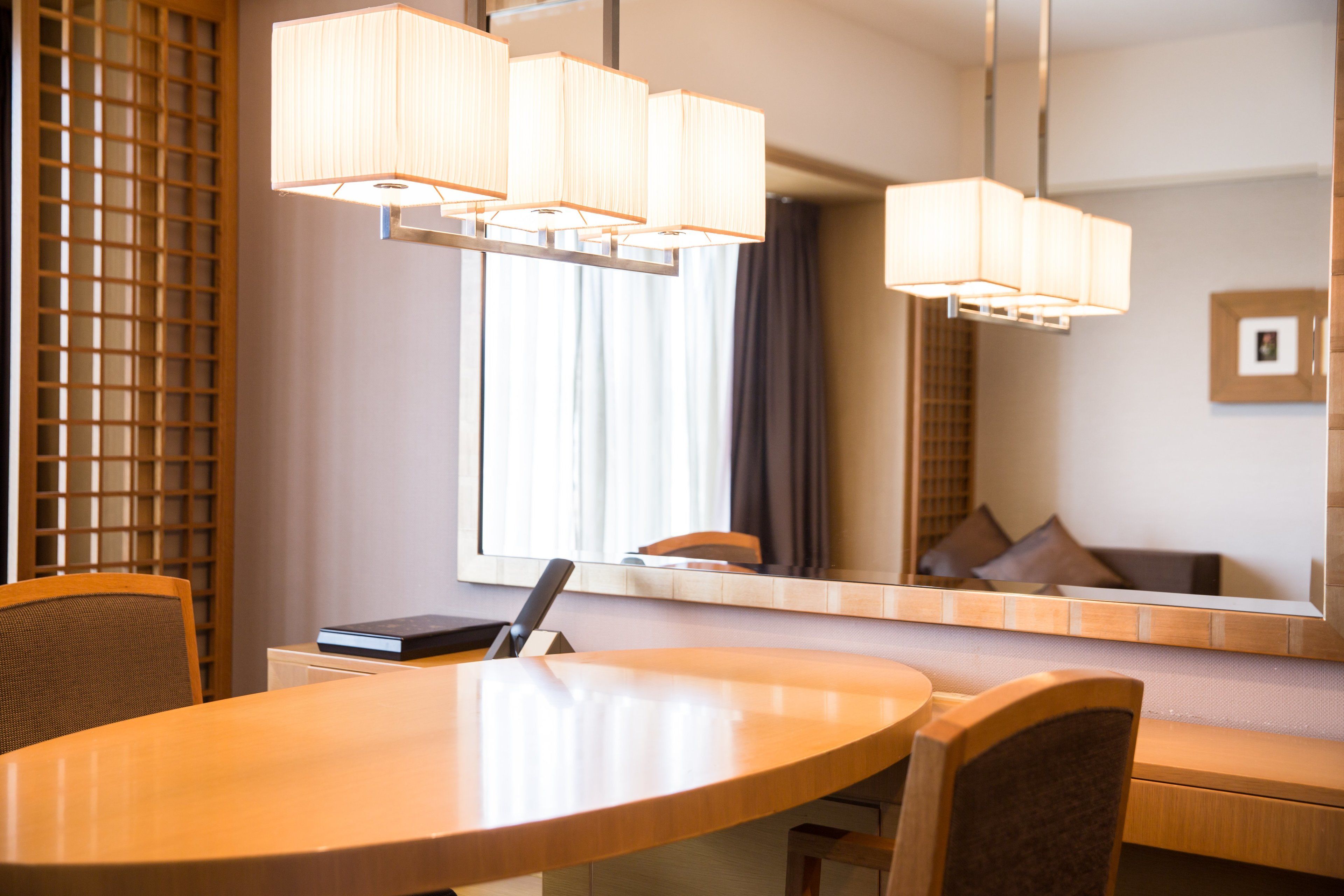 A hotel dining area with a round table, chairs, a book on the table, and a large mirror reflecting the room.