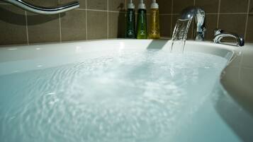 A bathtub with running water, a chrome faucet, and three bottles of liquid soap.