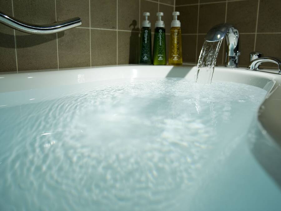 A bathtub with running water, a chrome faucet, and three bottles of liquid soap.