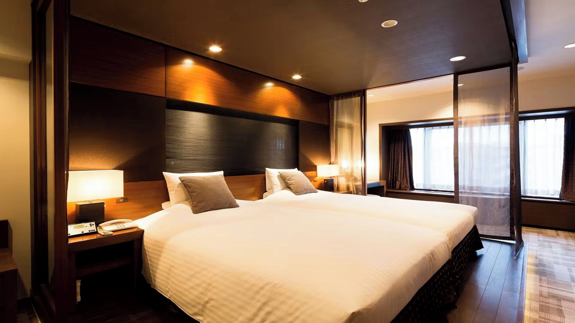 A large bed with a headboard, bedside tables with lamps, and a view of the outside through a window.