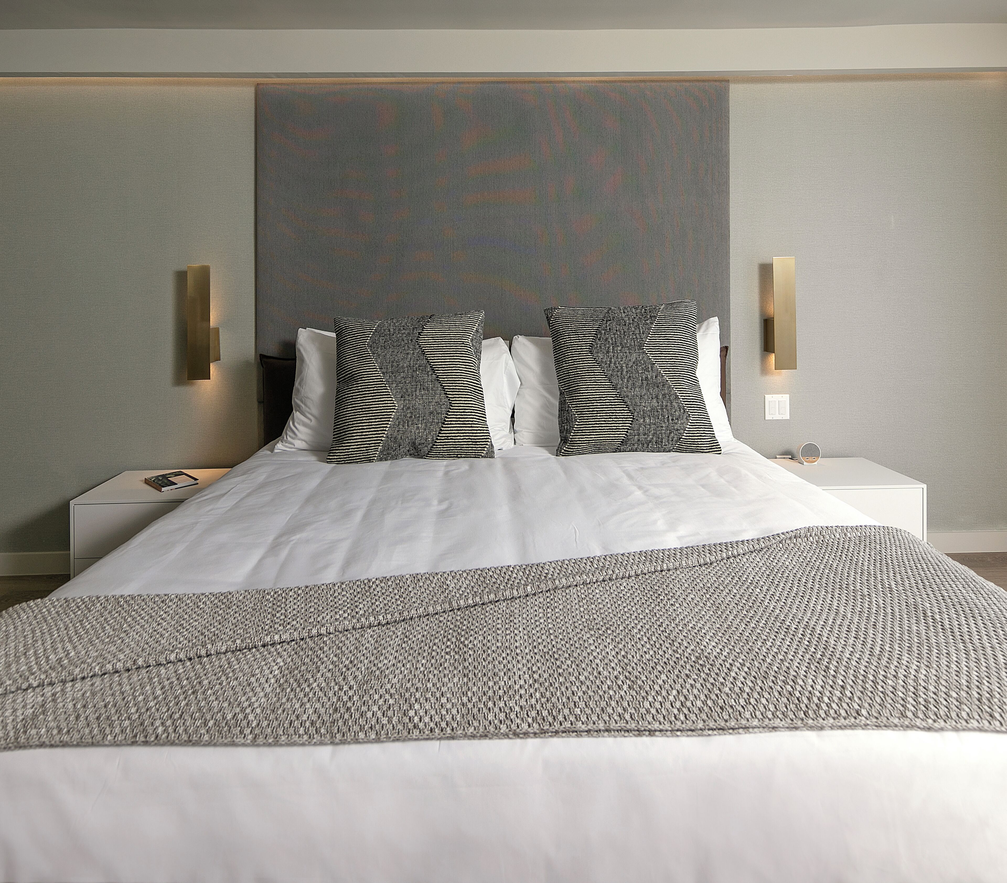 A modern hotel room with a large bed, two bedside tables, and a large wall-mounted artwork.
