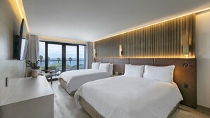 A modern hotel room with two beds, a desk, and a large window offering a view of the sea. - La Jolla Cove Suites (La Jolla)