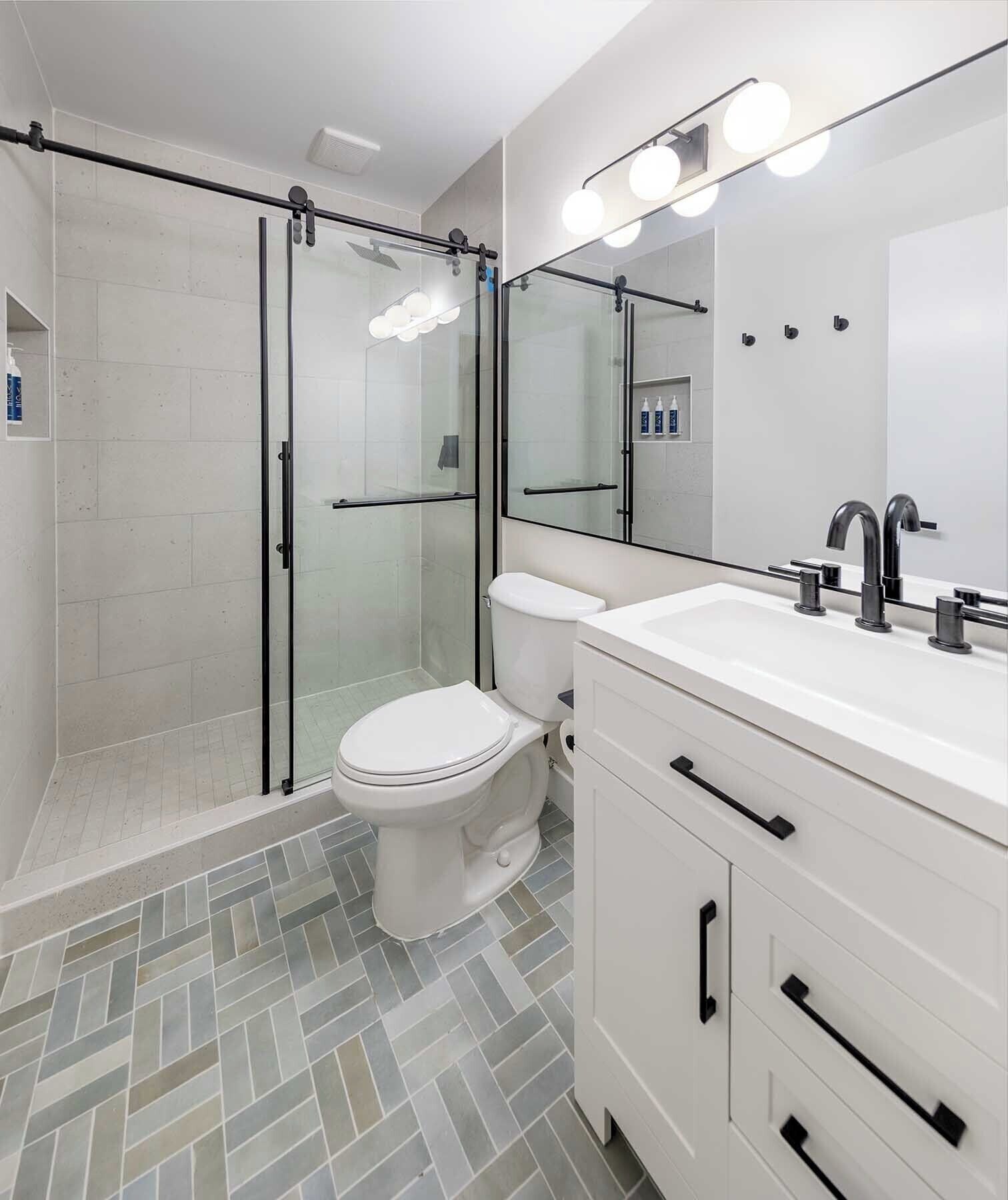 A modern bathroom with a glass-enclosed shower, a white toilet, and a vanity with a mirror and lights.
