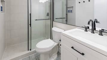 A modern bathroom with a glass-enclosed shower, a white toilet, and a vanity with a mirror and lights.