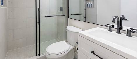 A modern bathroom with a glass-enclosed shower, a white toilet, and a vanity with a mirror and lights.