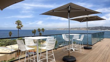 Une terrasse avec des chaises et des tables blanches, d’où l’on a une vue sur l’océan.
