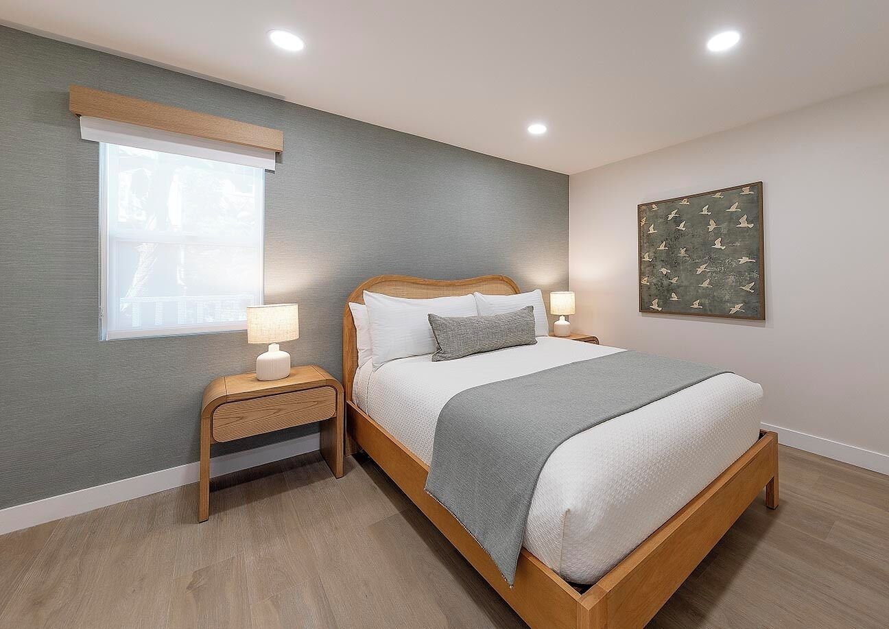 A bedroom with a bed, bedside tables, a window, and a wall-mounted artwork.