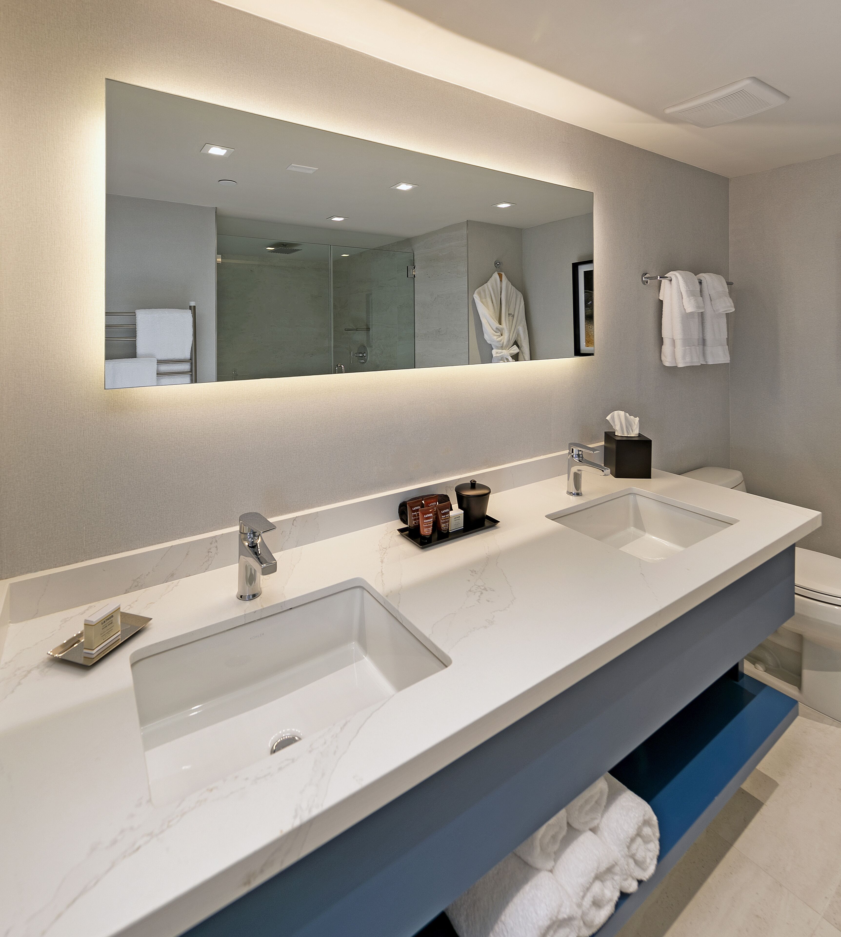 Une salle de bain moderne avec un grand miroir, deux lavabos et un porte-serviettes.