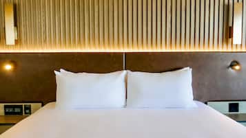 A neatly made bed with white linens and two pillows, a wooden slatted headboard, and two wall-mounted light fixtures.
