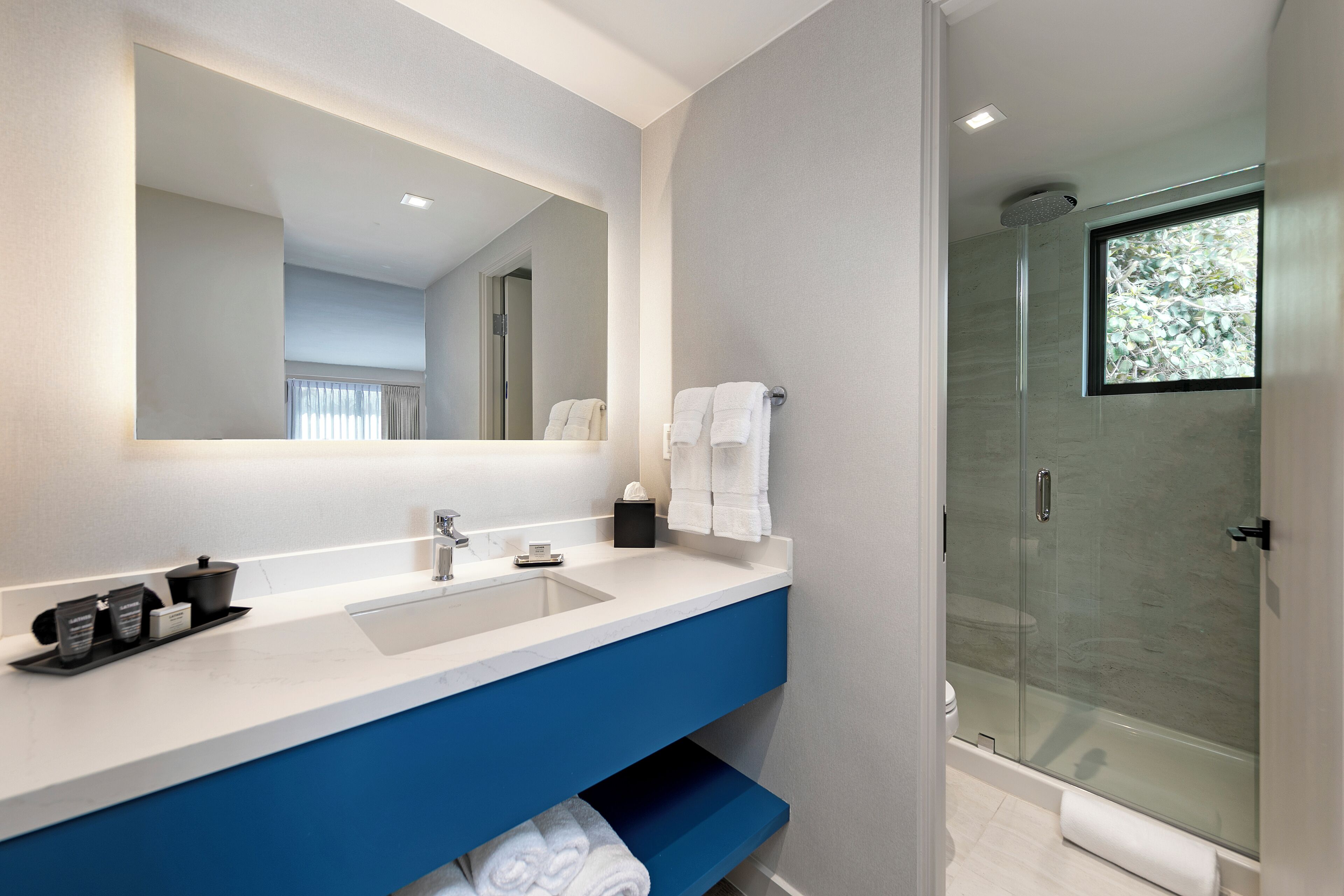 A modern bathroom with a large mirror, a dual sink vanity, a glass shower enclosure, and a visible toilet.