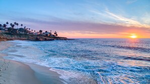 A beach with waves, a sunset, and a row of houses along the shore. - La Jolla Cove Suites (La Jolla)