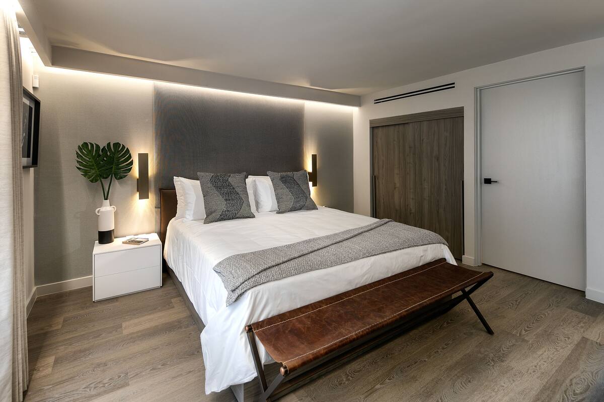A modern bedroom with a large bed, bedside tables, a bench, and a potted plant.