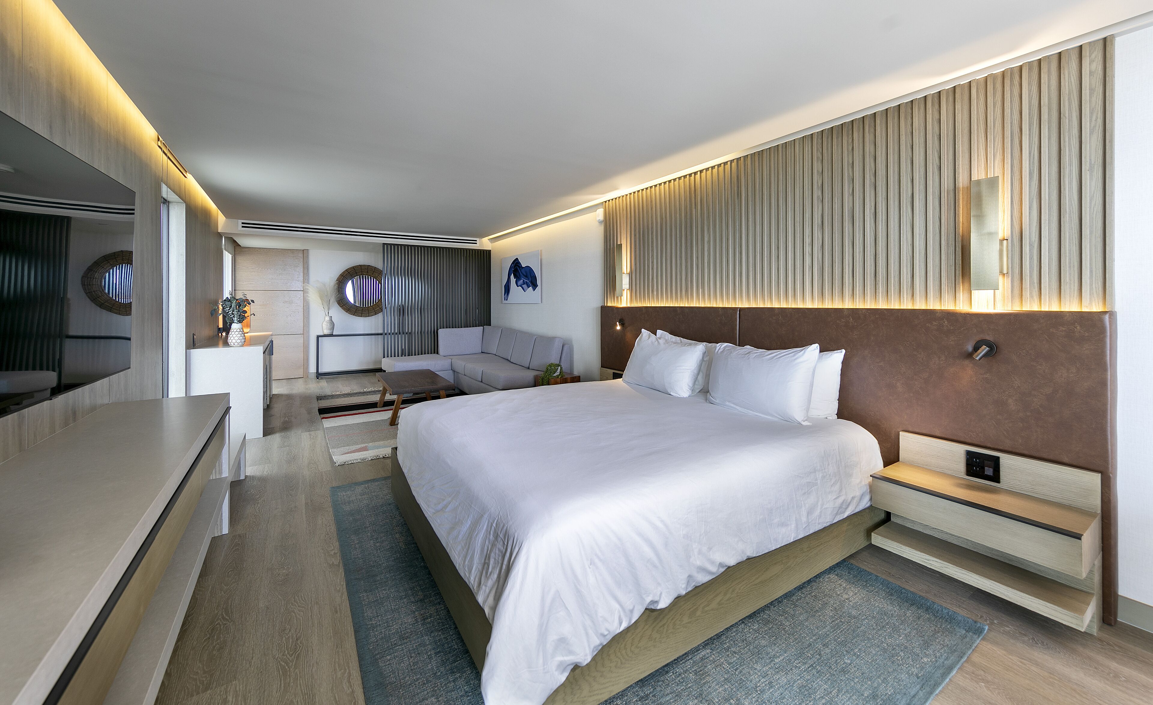 A modern hotel room with a large bed, a sofa, a desk, and a TV.