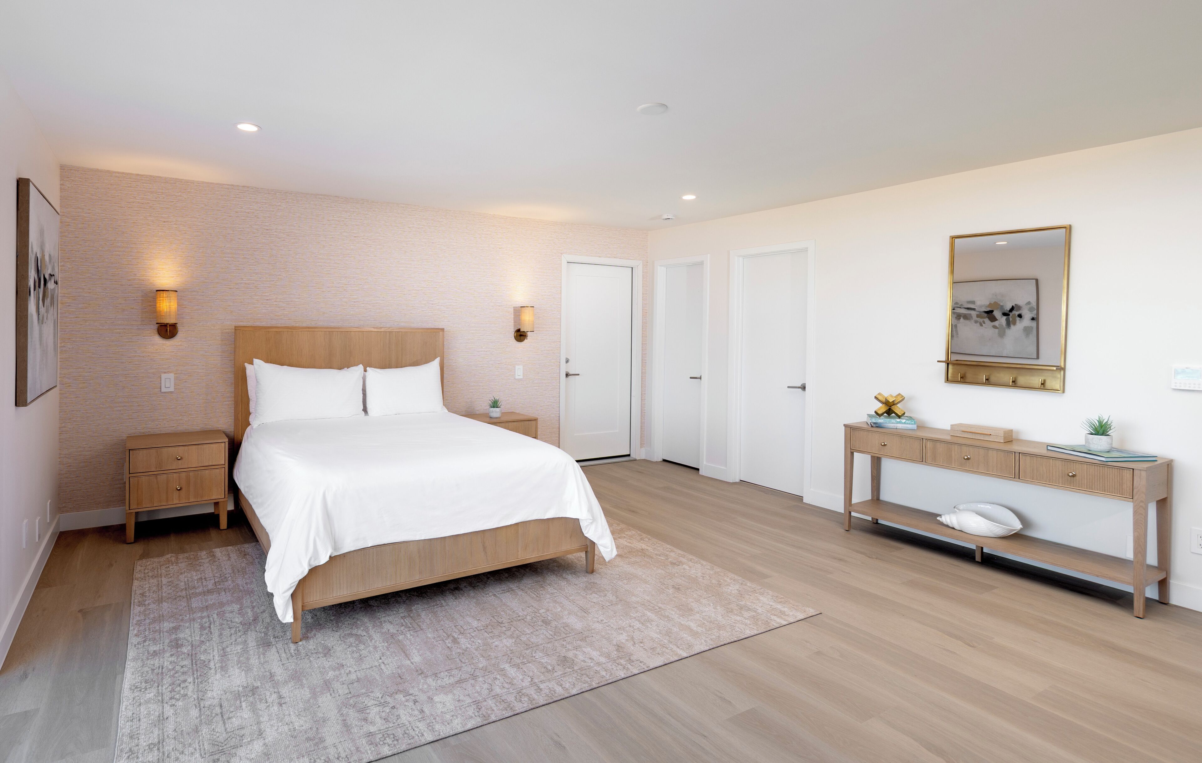 A modern bedroom with a wooden bed, bedside tables, a console table with a mirror, and a small plant.
