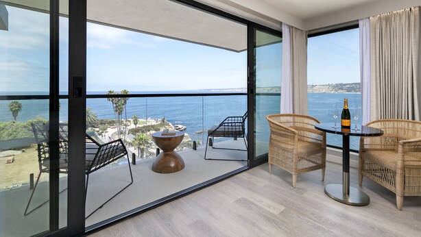 A balcony with a view of the ocean, wicker chairs, a round table, and a bottle of champagne. - La Jolla Cove Suites (La Jolla)