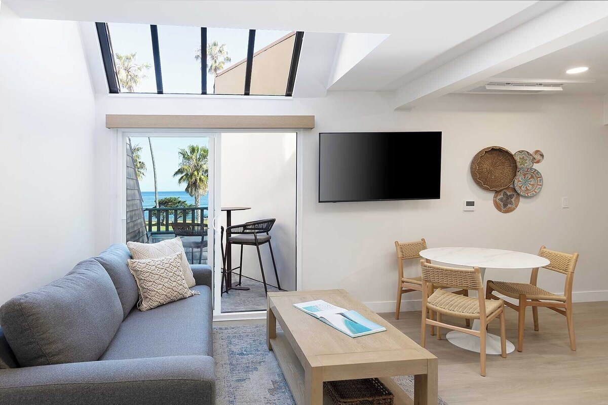 A modern living room with a sofa, coffee table, TV, and a balcony with a view.