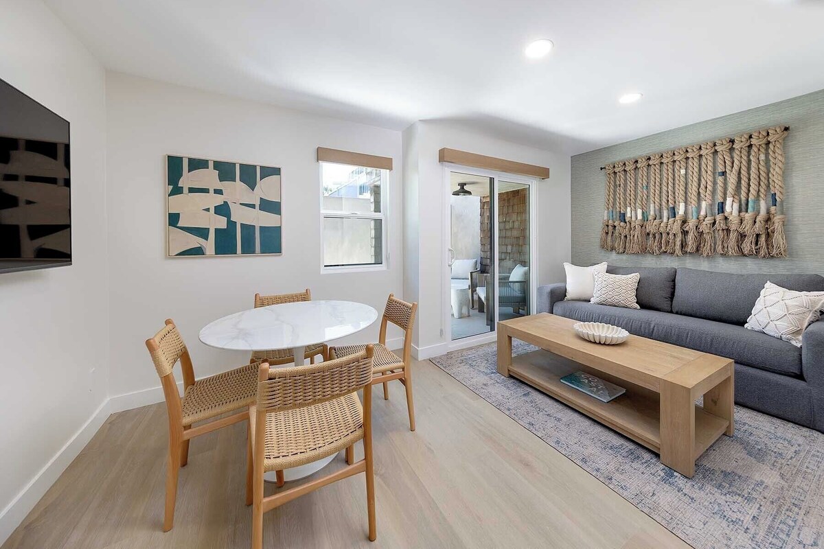 A modern living room with a round dining table, wicker chairs, a grey sofa, and a wooden coffee table.