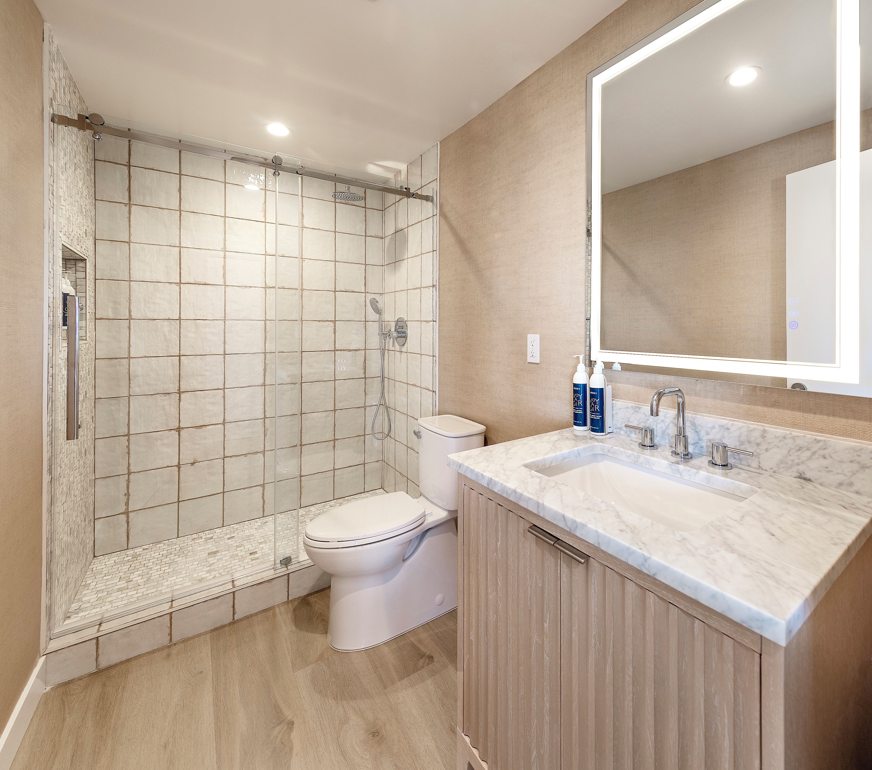 Un baño moderno con ducha, inodoro y tocador con espejo.