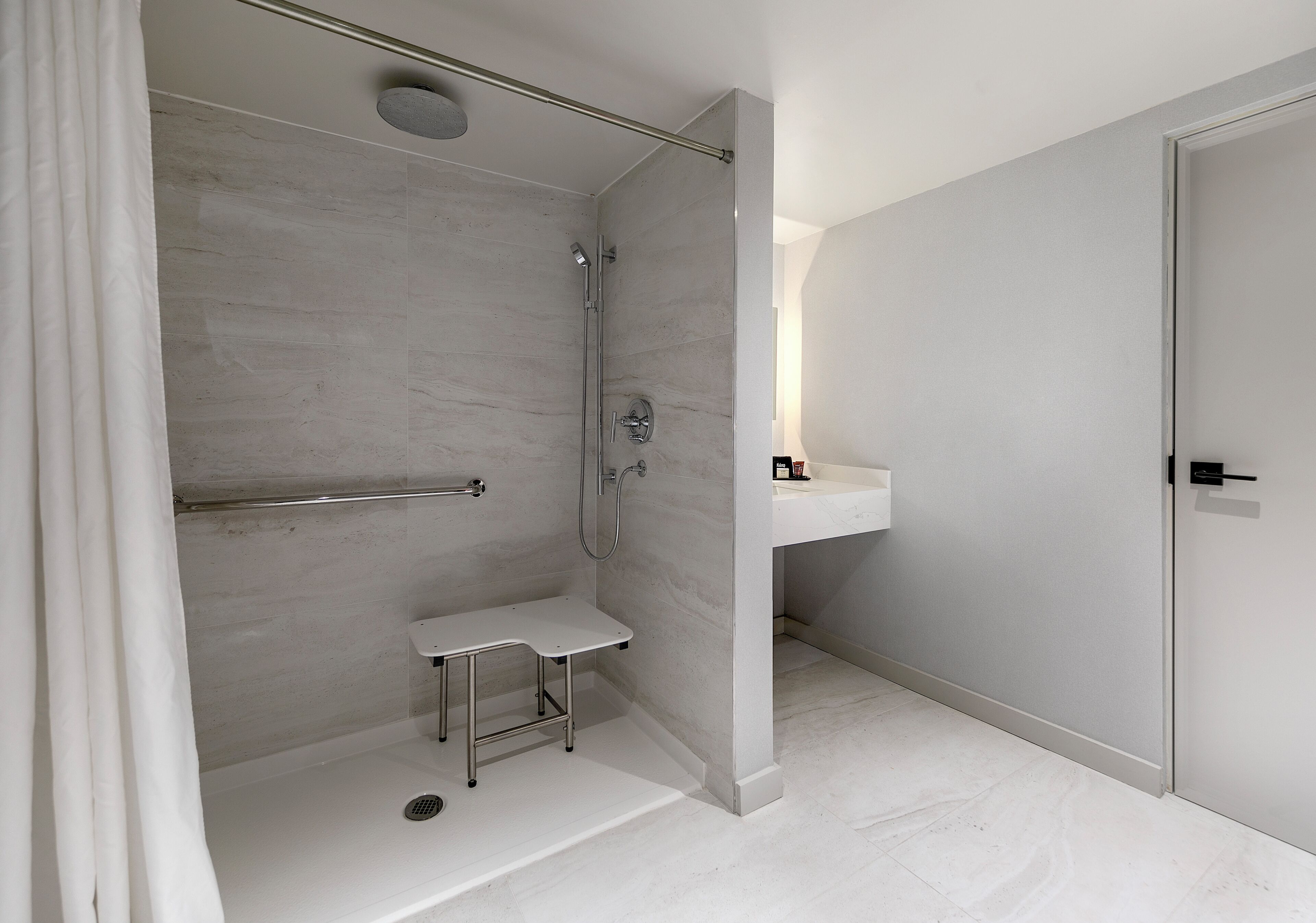 Un baño moderno con cabina de ducha, un taburete pequeño y un lavamanos con espejo.