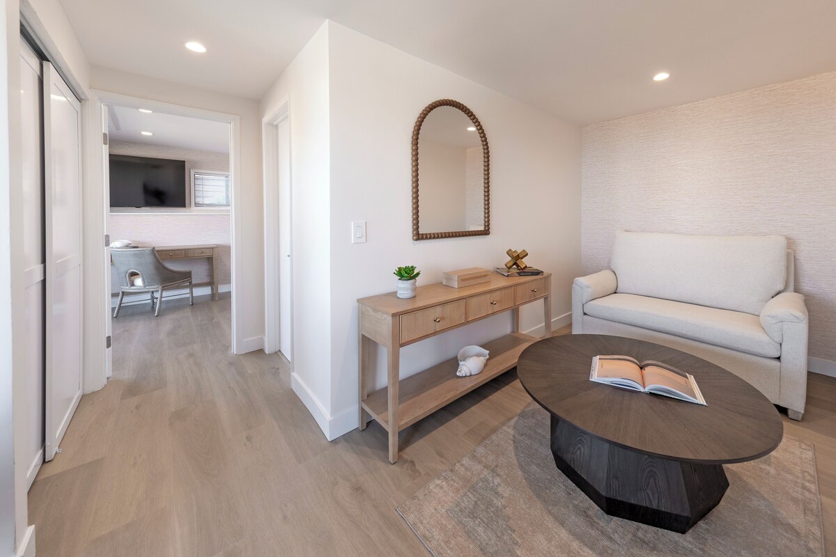 A modern living room with a sofa, a coffee table with a book, a wooden console table, and a mirror on the wall.