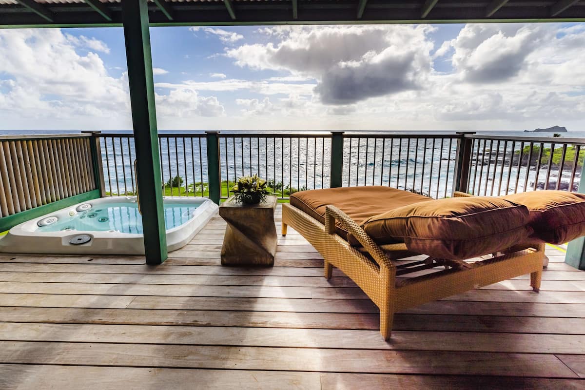 A wooden deck with a hot tub, wicker sofa, and a view of the ocean.