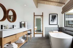 A modern bathroom with a large bathtub, a wooden vanity with a mirror, and a shower area.