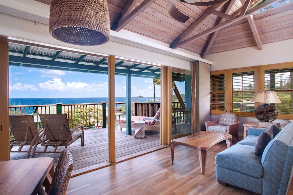 A wooden deck with outdoor seating, large windows, and a view of the ocean.