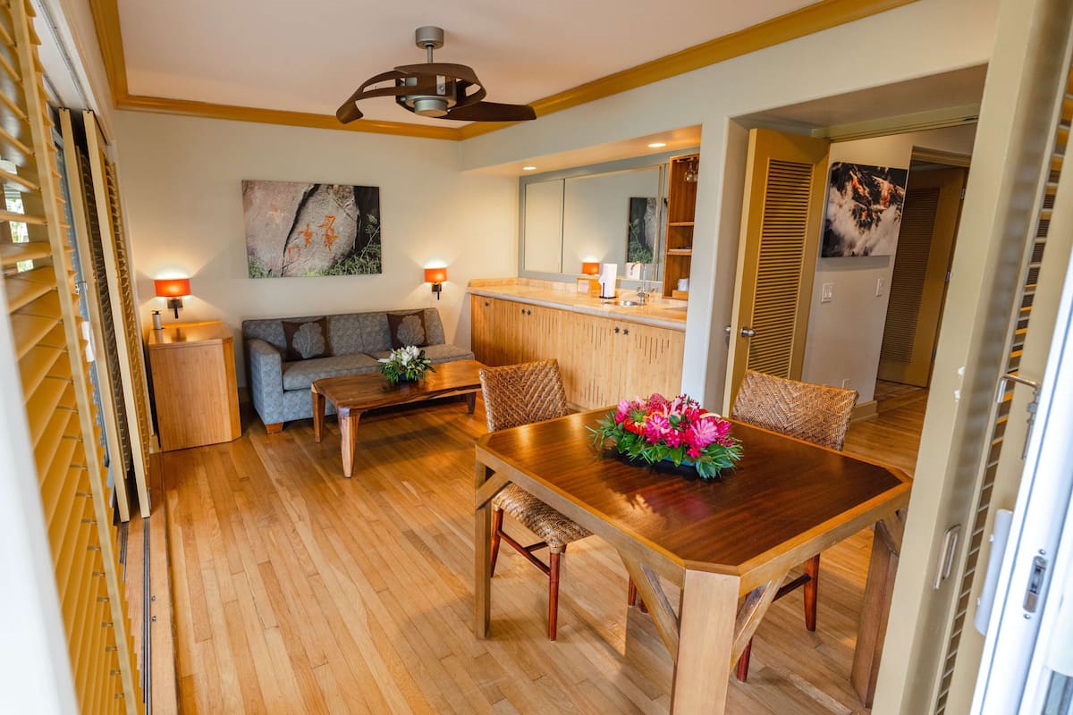 A modern kitchen with wooden cabinets, a dining table with chairs, and a sofa in the living area.