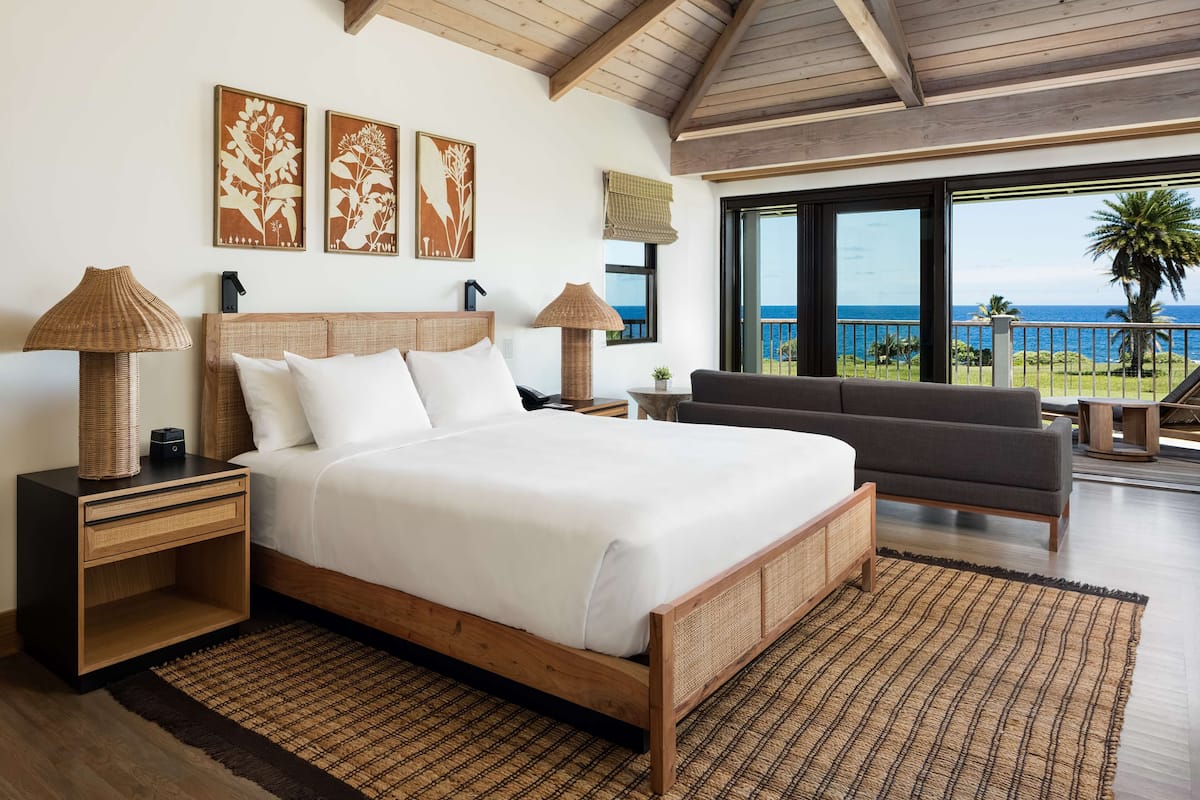 A bedroom with a large bed, two nightstands, a sofa, and a view of the ocean.