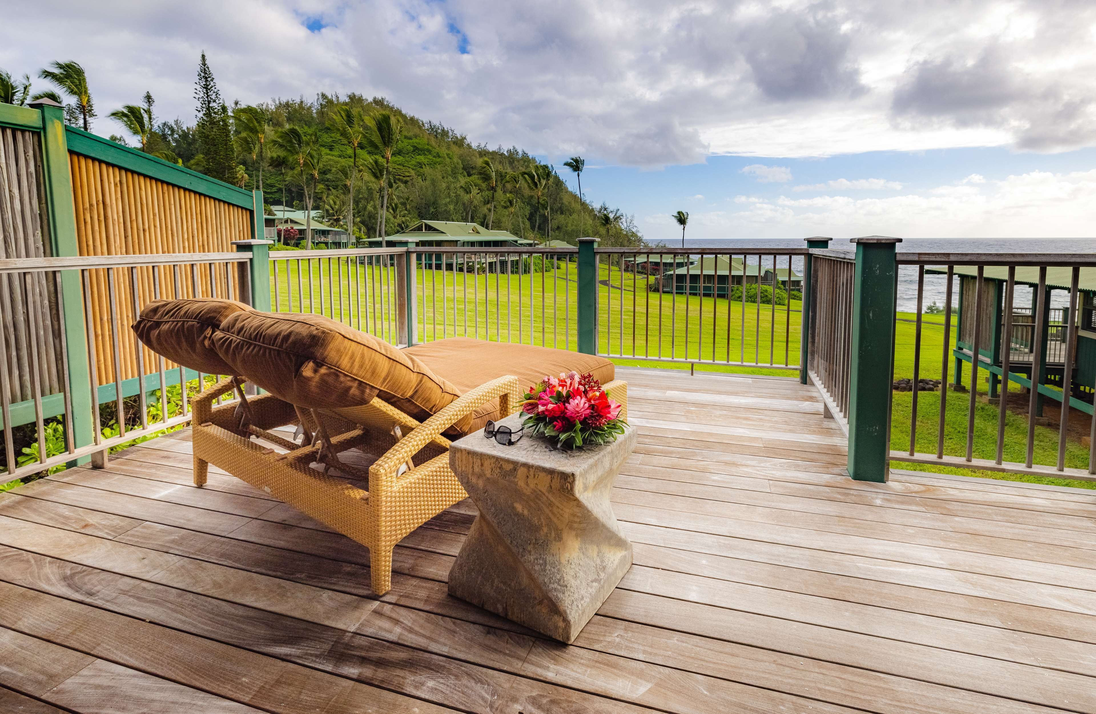 A wooden deck with a wicker lounge chair and a stone table with a flower arrangement and glasses.