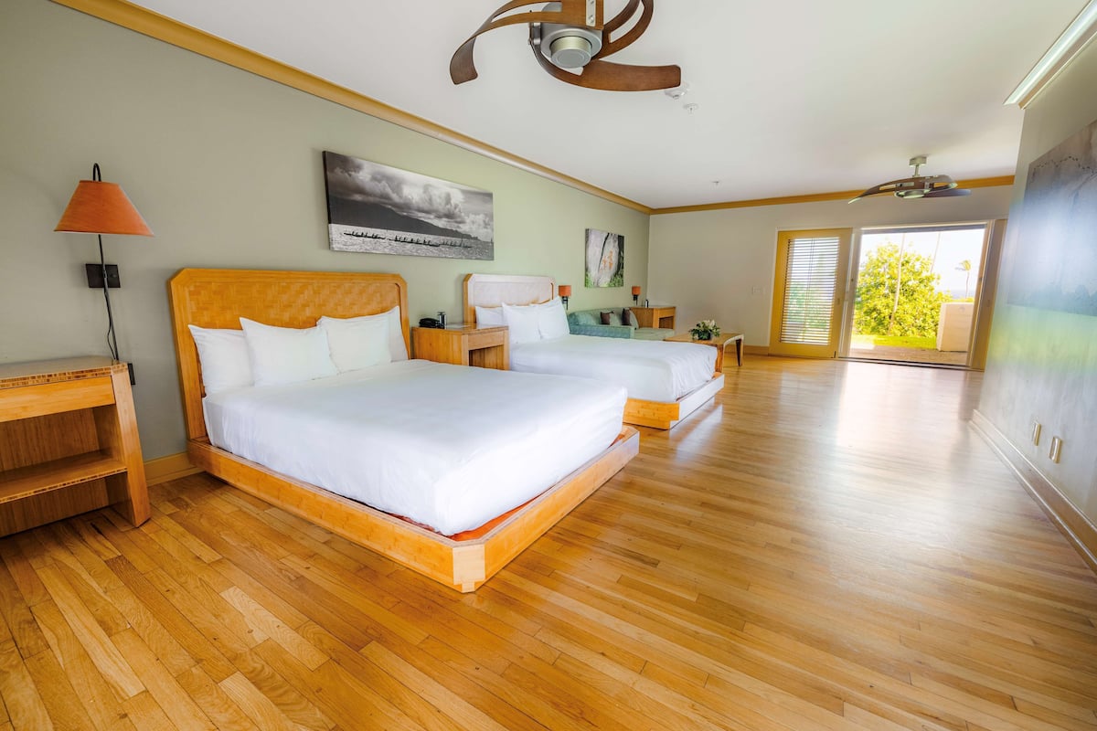 A spacious bedroom with two wooden beds, a large window, and a ceiling fan.