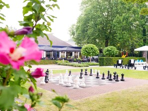 A chessboard set outdoors with tables and chairs in the background.