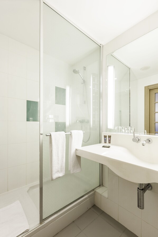 A modern bathroom with a glass shower enclosure, a white sink, and a large mirror. - Novotel Breda (Breda)