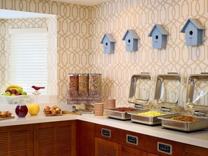 A breakfast buffet with various food items, a fruit bowl, and decorative birdhouses on the wall. - Sonesta ES Suites Omaha (Omaha)