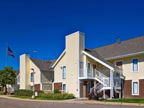 A multi-story residential building with a central staircase, a flagpole with an American flag, and a well-maintained lawn. - Sonesta ES Suites Omaha (Omaha)