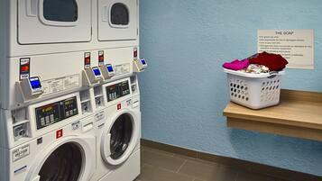 A laundry room with stacked washers and dryers, a payment terminal, and a basket of laundry on a shelf.