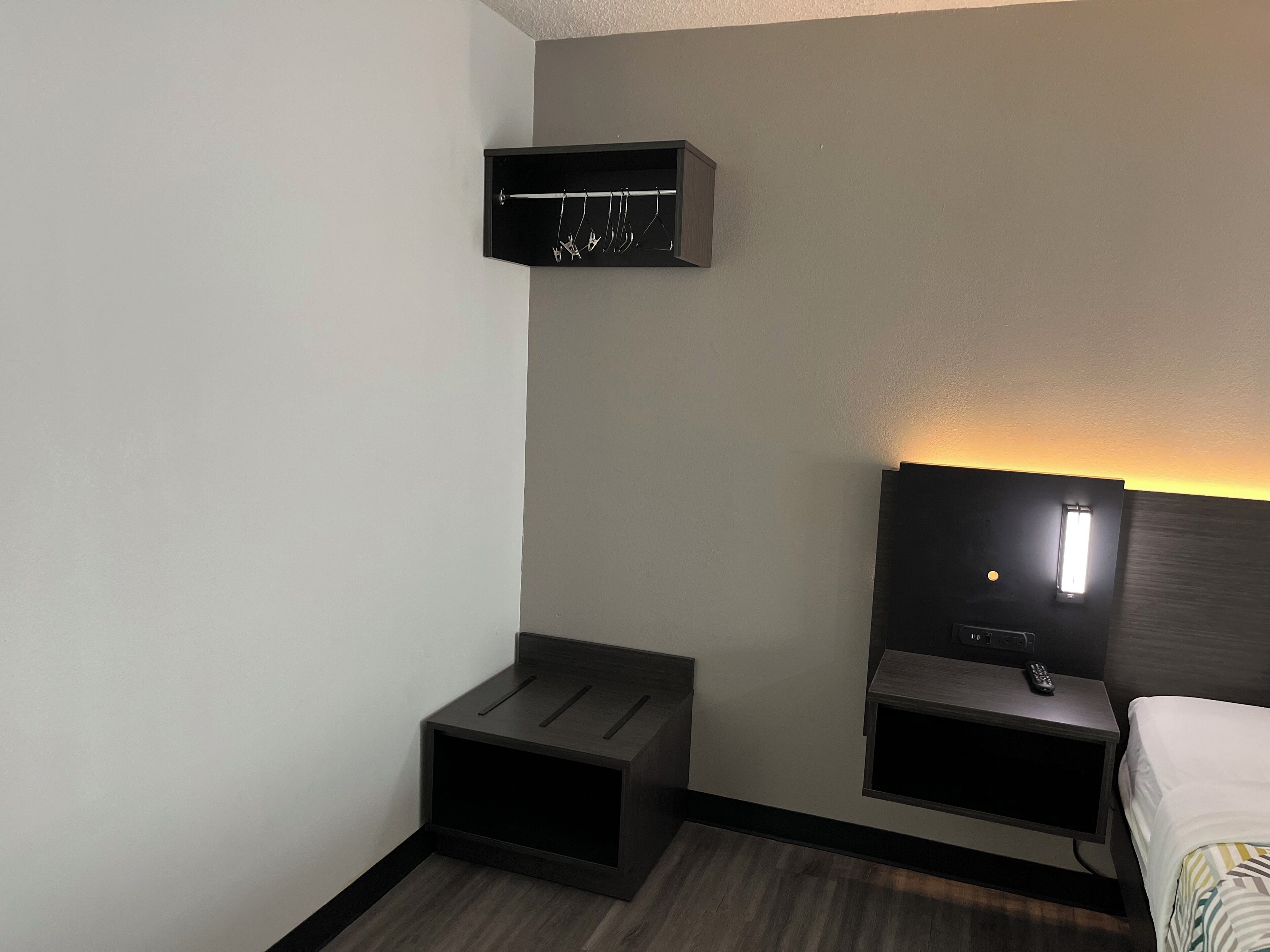 A hotel room with a bed, a nightstand with a lamp, a small table, and a coat rack.