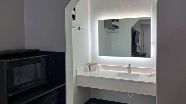 Une petite salle de bain avec un meuble-lavabo blanc, un grand miroir et un four à micro-ondes encastré.