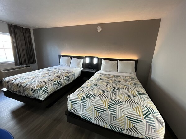 A hotel room with two beds, each with a patterned bedspread, a nightstand with a lamp, and a window with curtains.