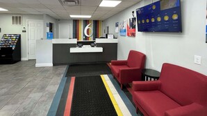 Un espace d’accueil avec un comptoir, un grand panneau portant le chiffre « 6 », un coin salon avec des chaises rouges et un écran affichant les prévisions météorologiques au mur.