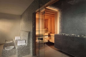 A modern bathroom with a glass-enclosed shower, a wicker sofa with towels, and a stone-tiled wall. - Lindner Hotel Cologne City Plaza, part of JdV by Hyatt (Cologne)
