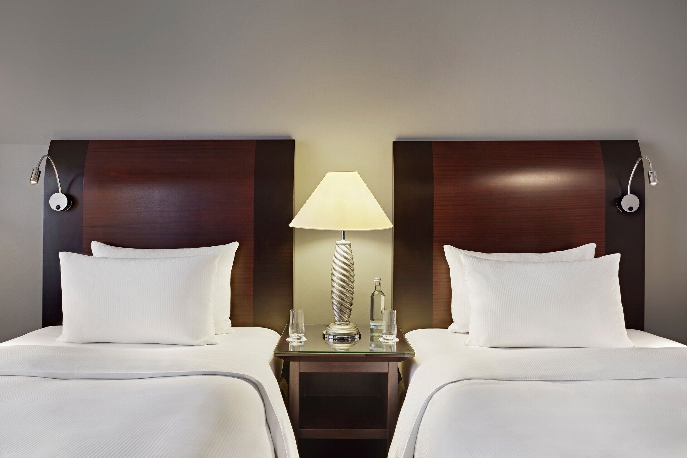 A hotel room with two beds, a bedside table with a lamp, and a bottle.