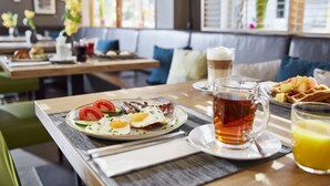 A breakfast setting with a plate of eggs, bacon, and tomatoes, a glass of tea, and a waffle.