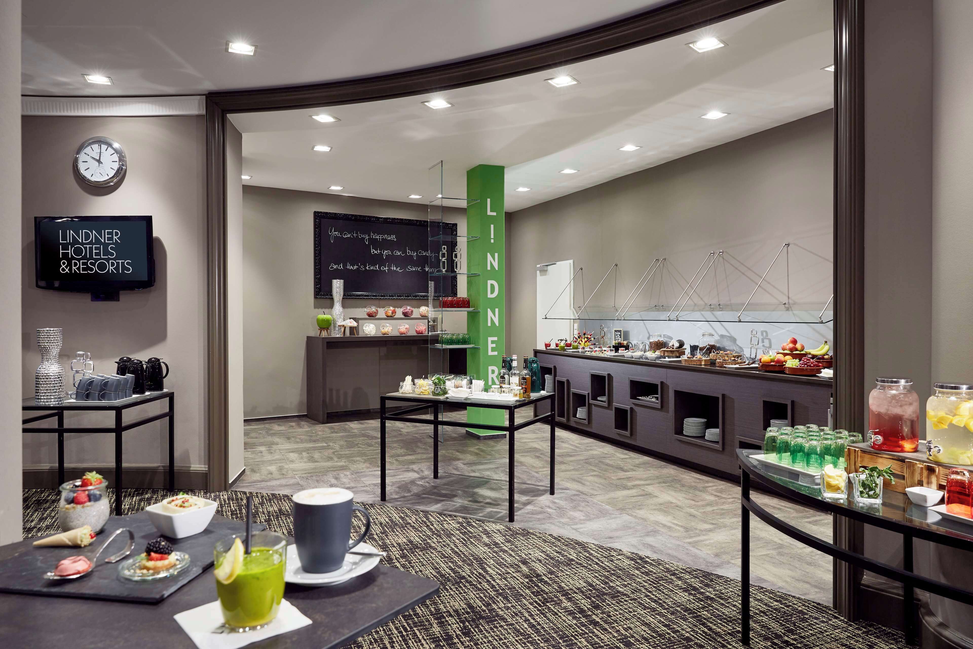 Un hall de hotel con zona de buffet, un reloj y una televisión que muestra el nombre del hotel.