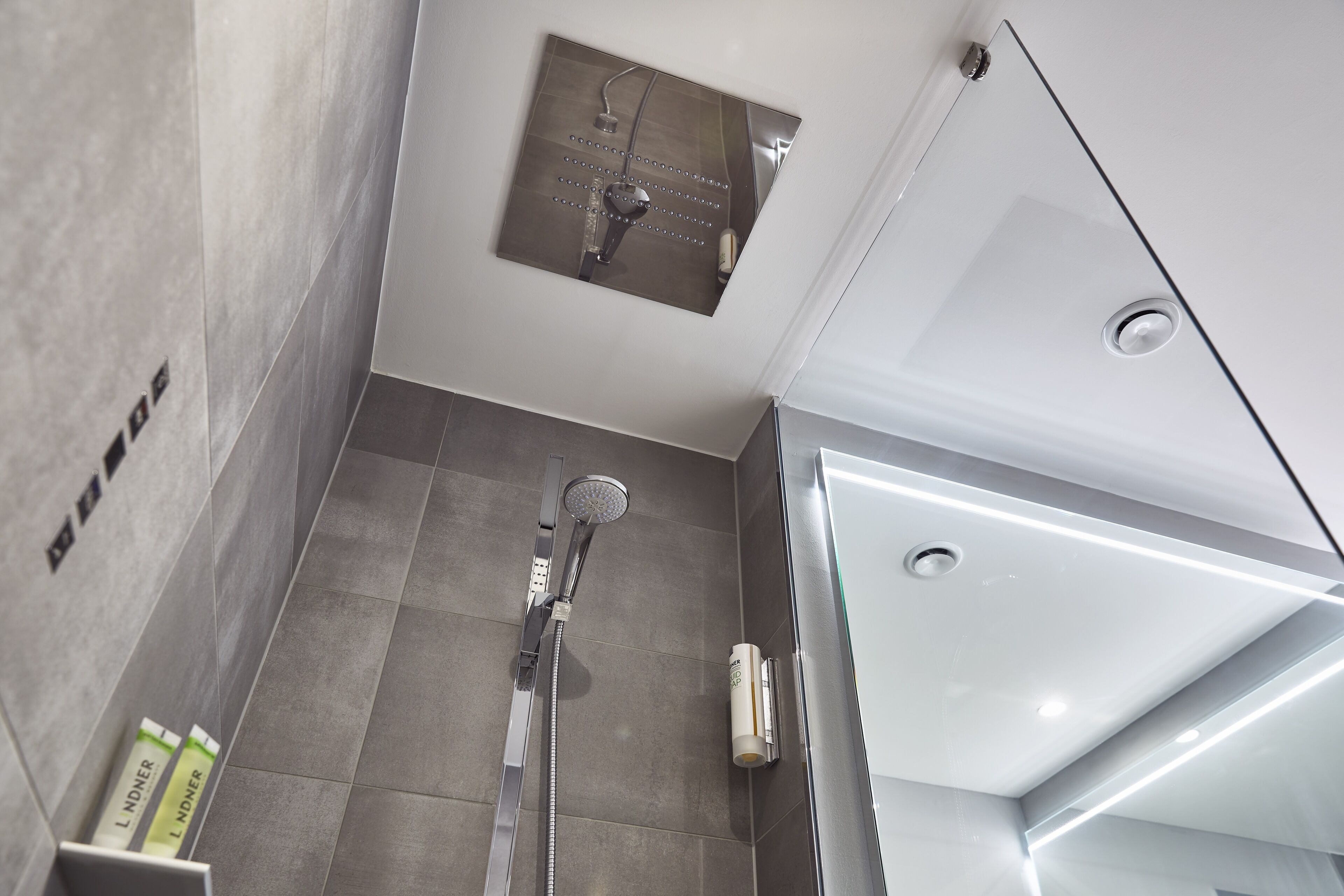 Un baño moderno con ducha, panel de control en la pared y cabina de vidrio.