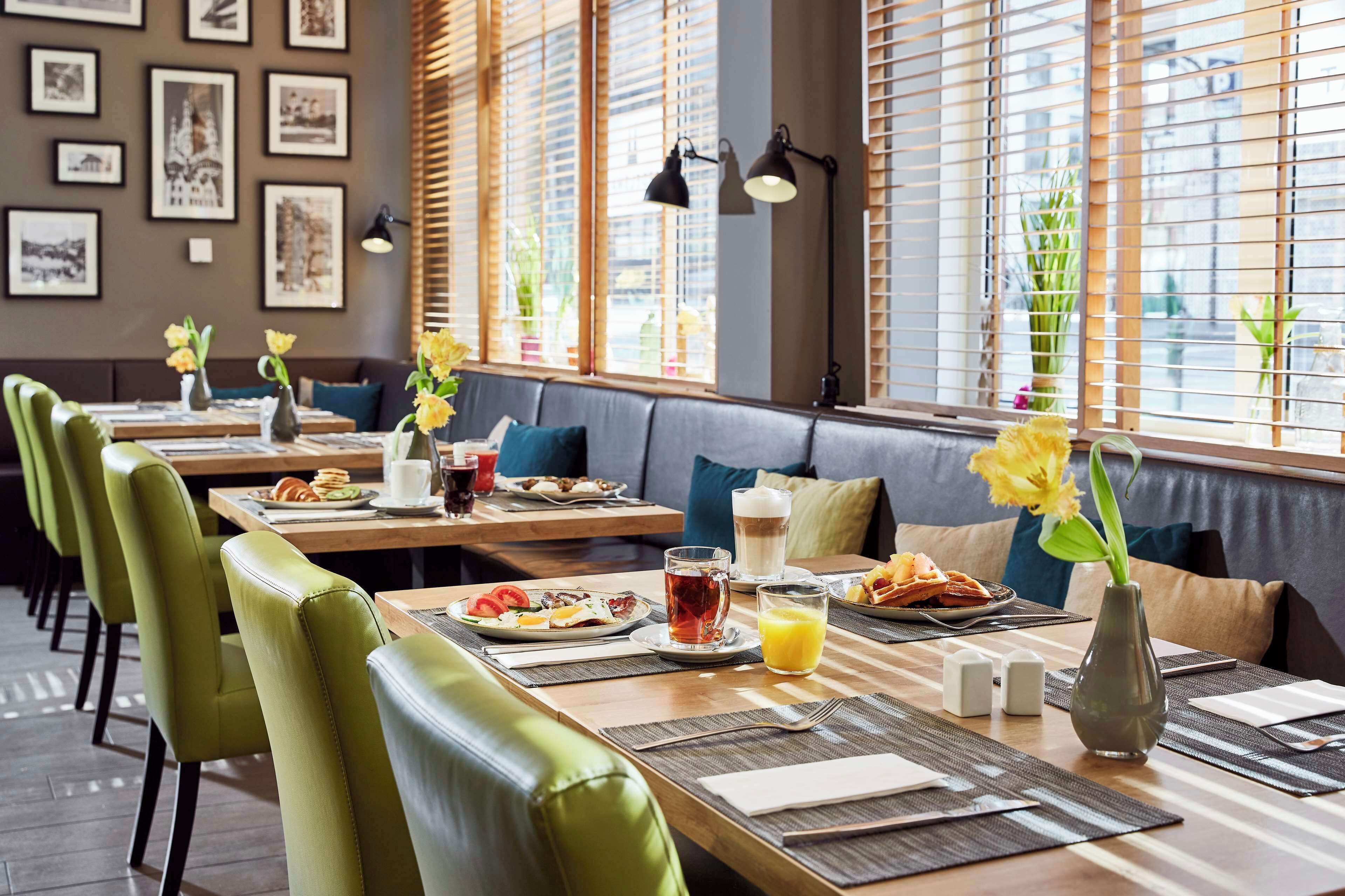 A restaurant with booths, green chairs, and tables set with plates, drinks, and flowers.