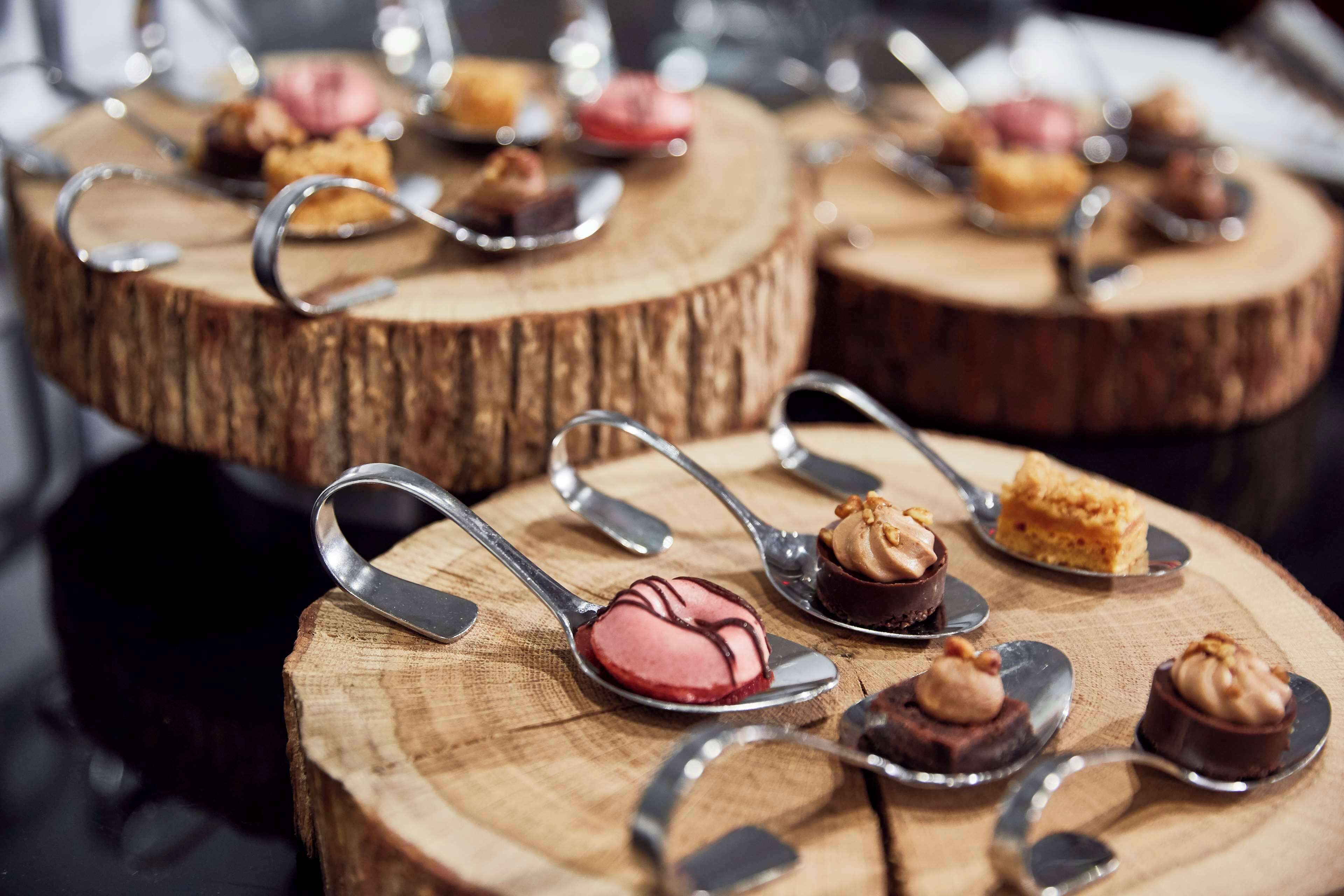 A variety of desserts on wooden serving boards with spoons.