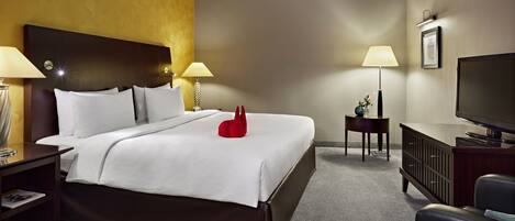 A hotel room with a large bed, two bedside tables with lamps, a television, and a small side table with a vase.