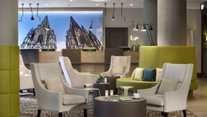 A modern hotel lobby with comfortable seating, a reception desk, and a large window with a view of a gothic-style building.
