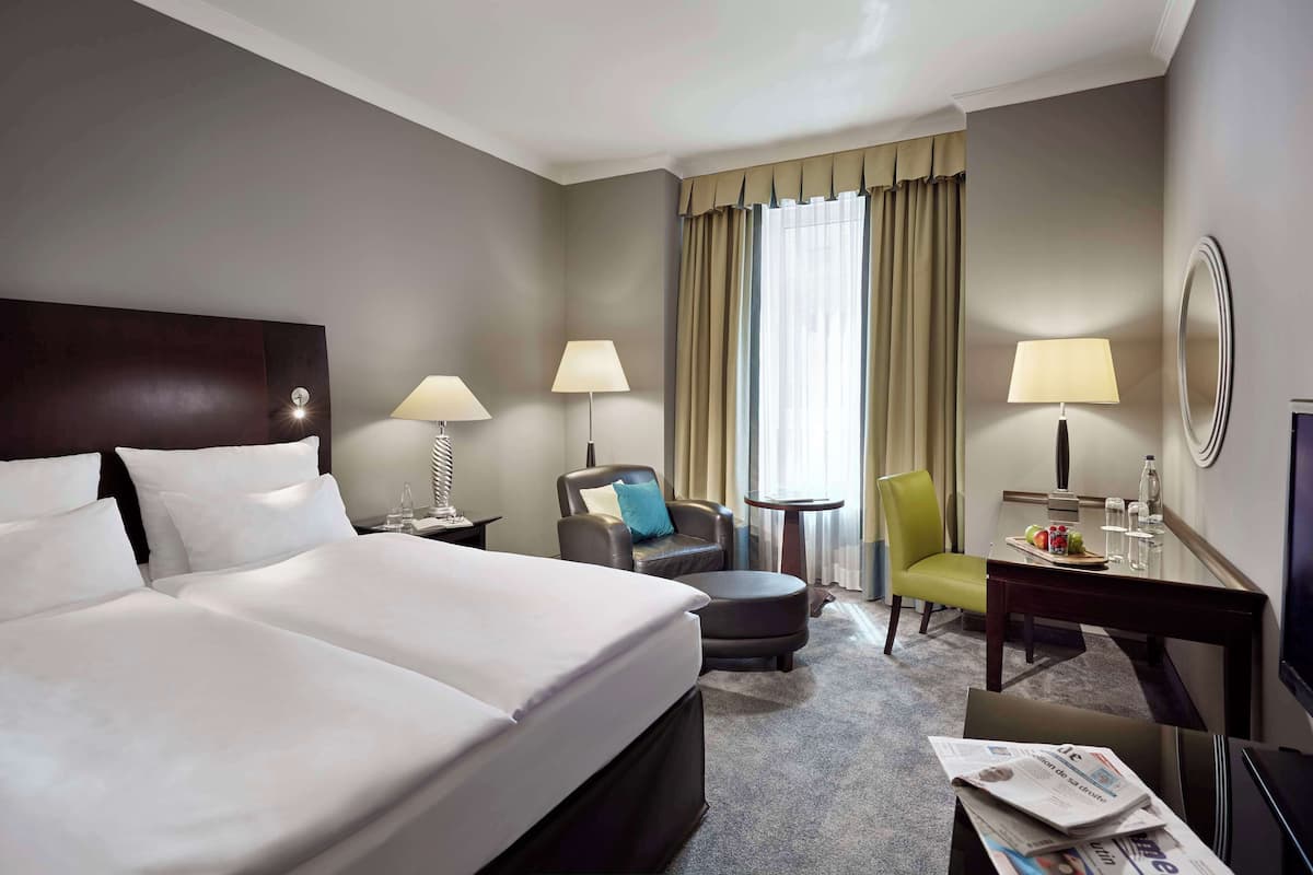 Ein Hotelzimmer mit einem großen Bett, zwei Nachttischen mit Lampen, einem Schreibtisch mit Stuhl, einem kleinen runden Tisch und einem Fernseher.
